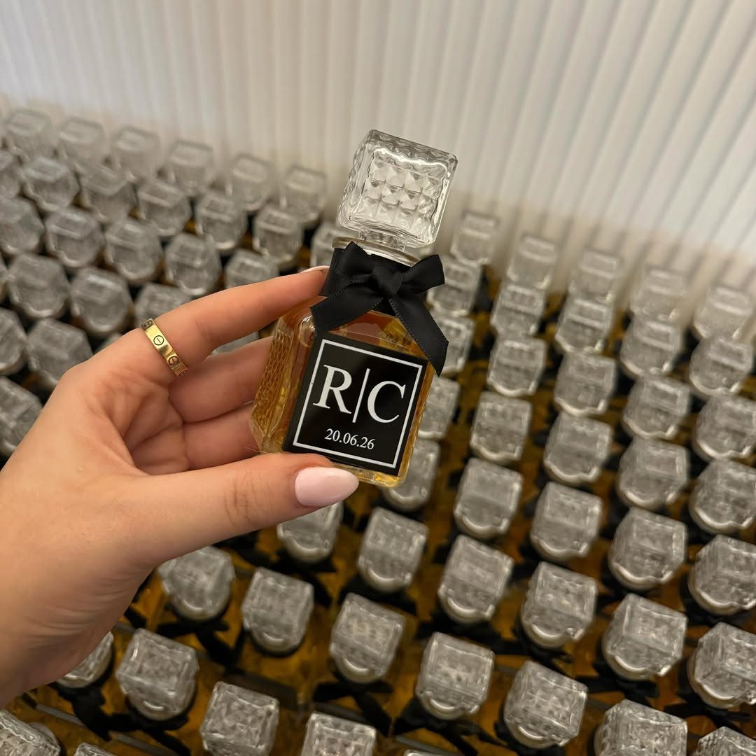 A hand holding a small personalized liquor bottle with a black bow and label.
