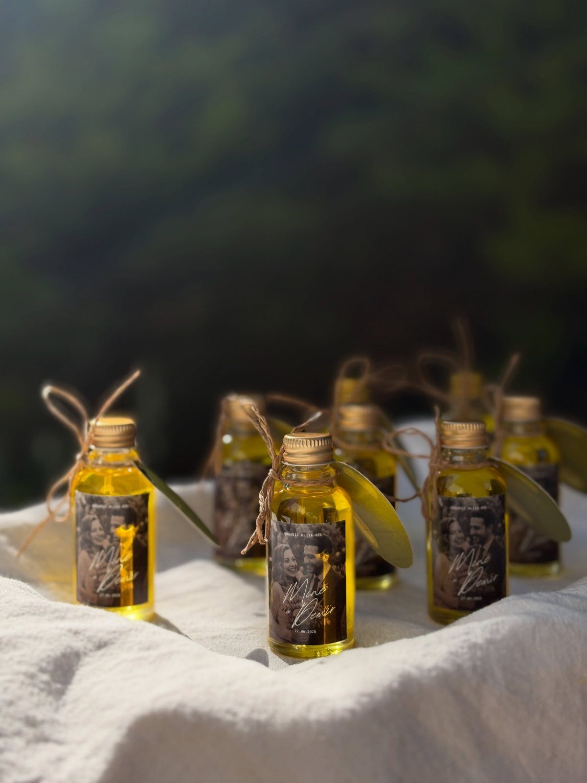Small glass bottles of golden olive oil with olive leaf accents on white linen.