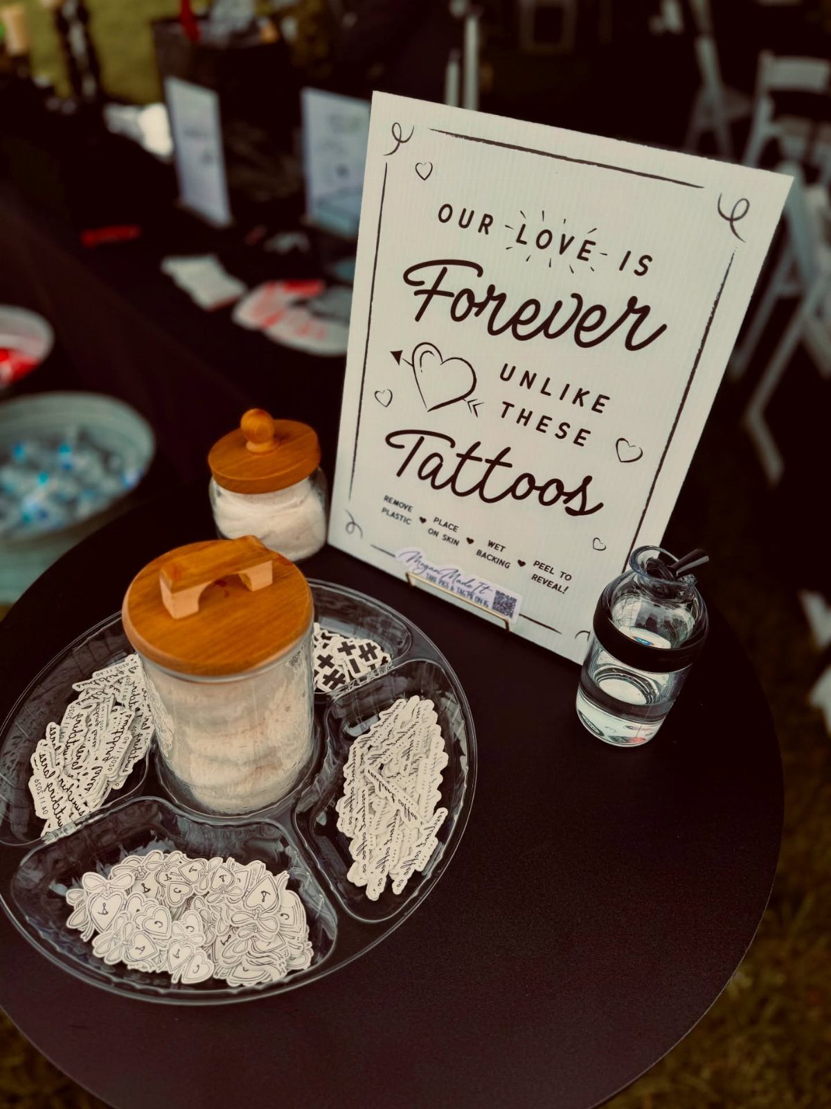 Temporary tattoo designs in a clear divided tray next to a decorative sign on a table.