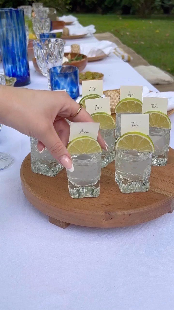 A hand reaches for a small shot glass with a lime slice and name card.