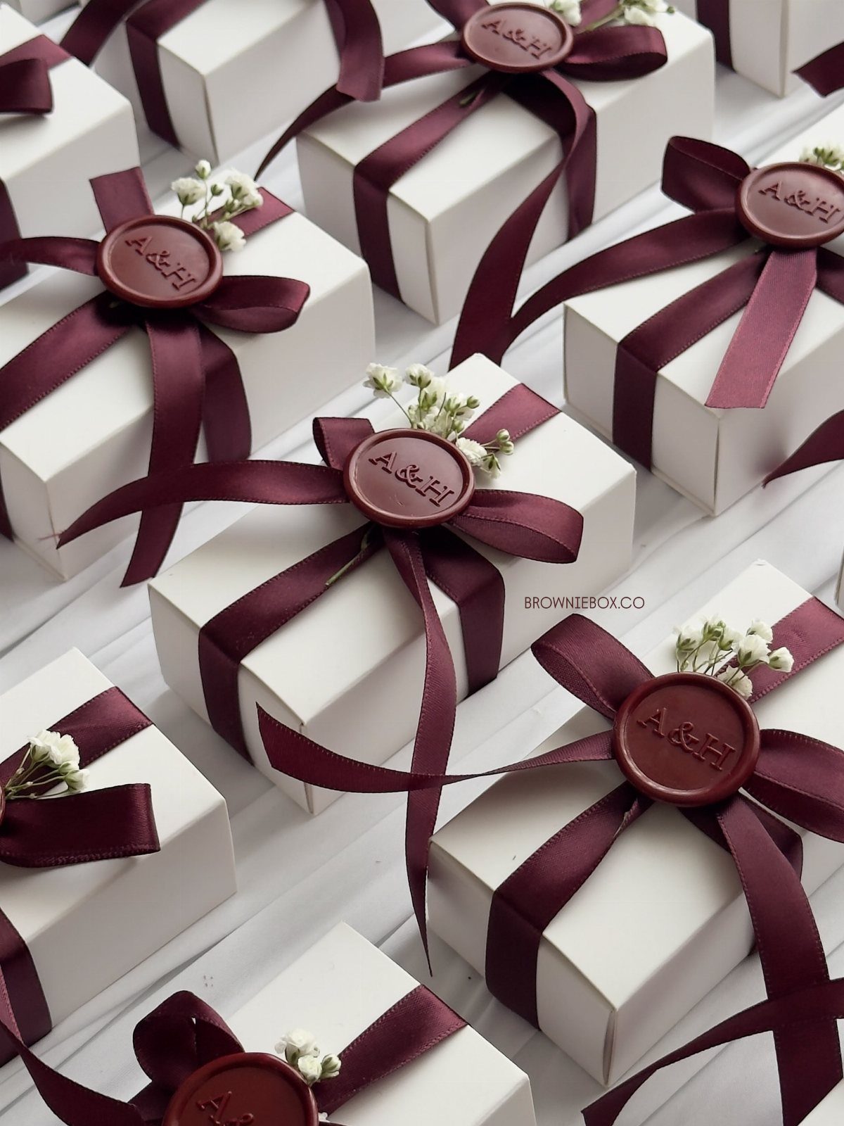 Small white gift boxes tied with burgundy ribbons and wax seals featuring initials.
