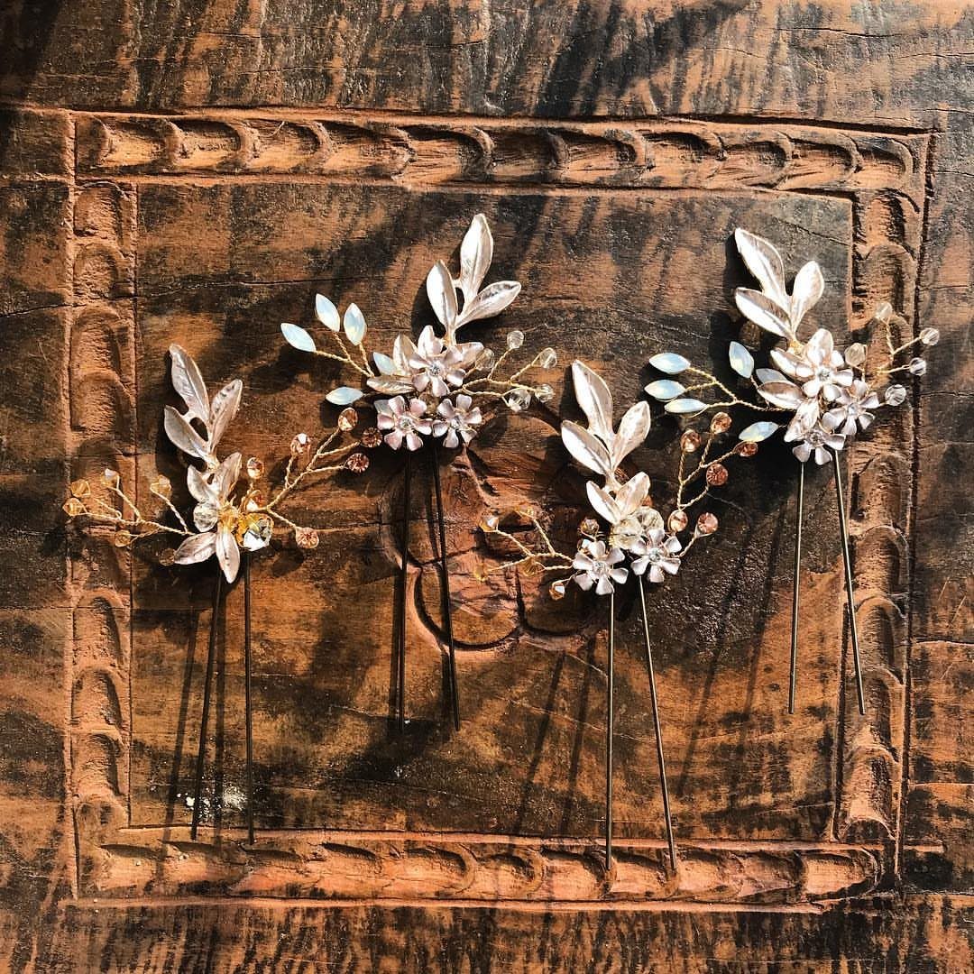 Four gold hair pins with leaves, pearls, and crystals resting on a carved wooden background.