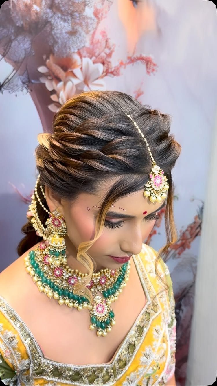 A woman wearing a gold maang tikka with a pink floral pendant on her forehead.
