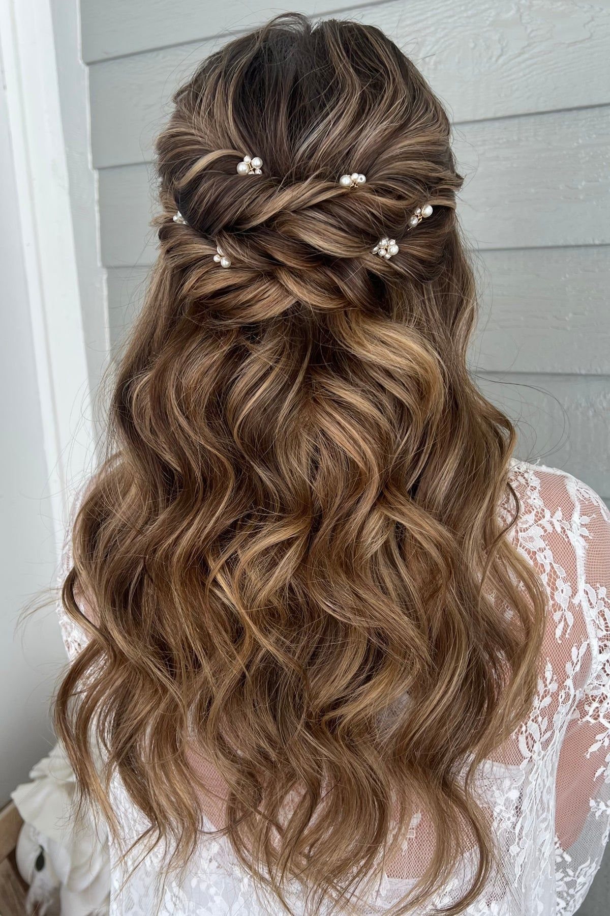 Long wavy brown hair styled in a half-updo decorated with small white pearl hair pins.