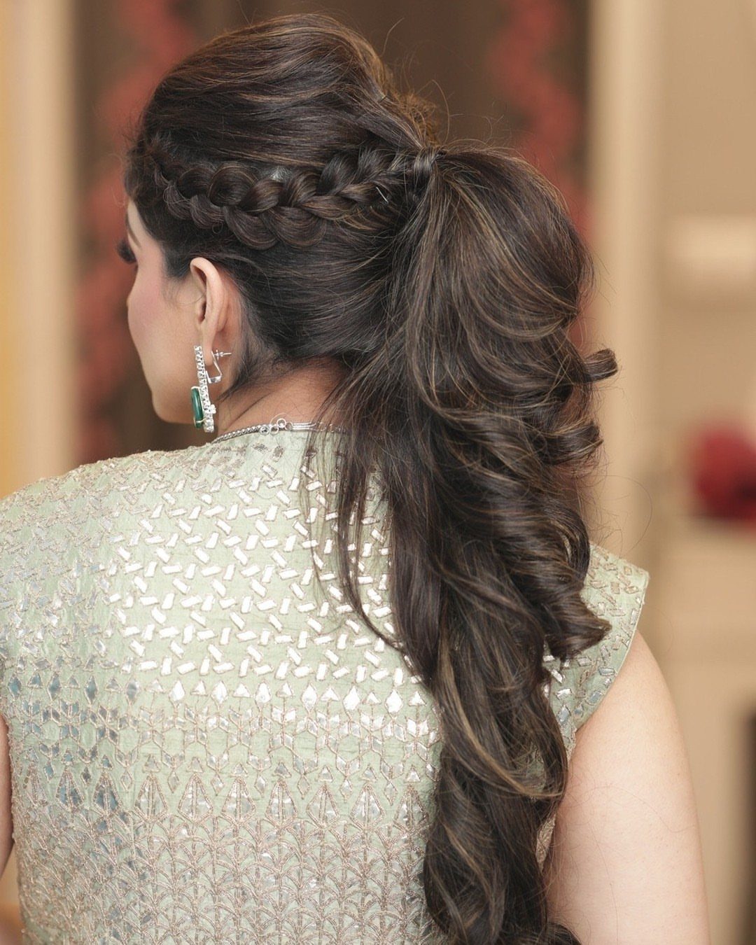 A woman with a thick braided ponytail and voluminous wavy hair cascading down her back.