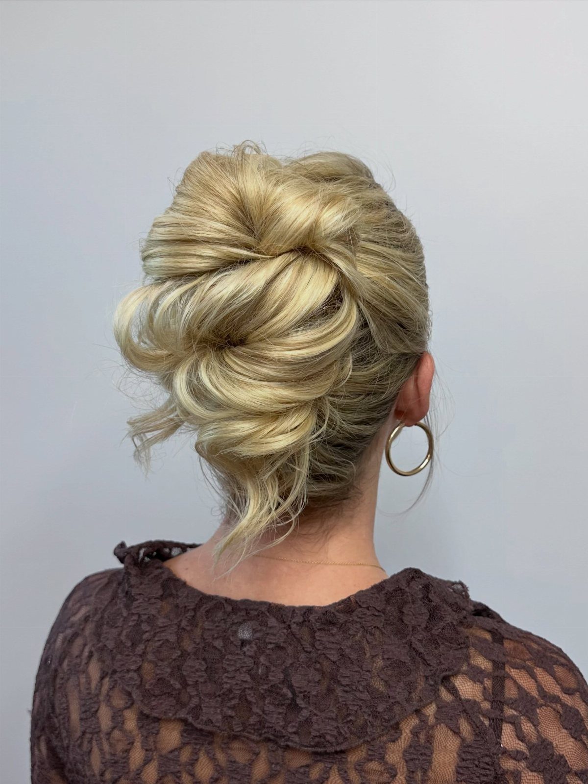 Blonde hair styled in a voluminous, textured chic updo against a light background.