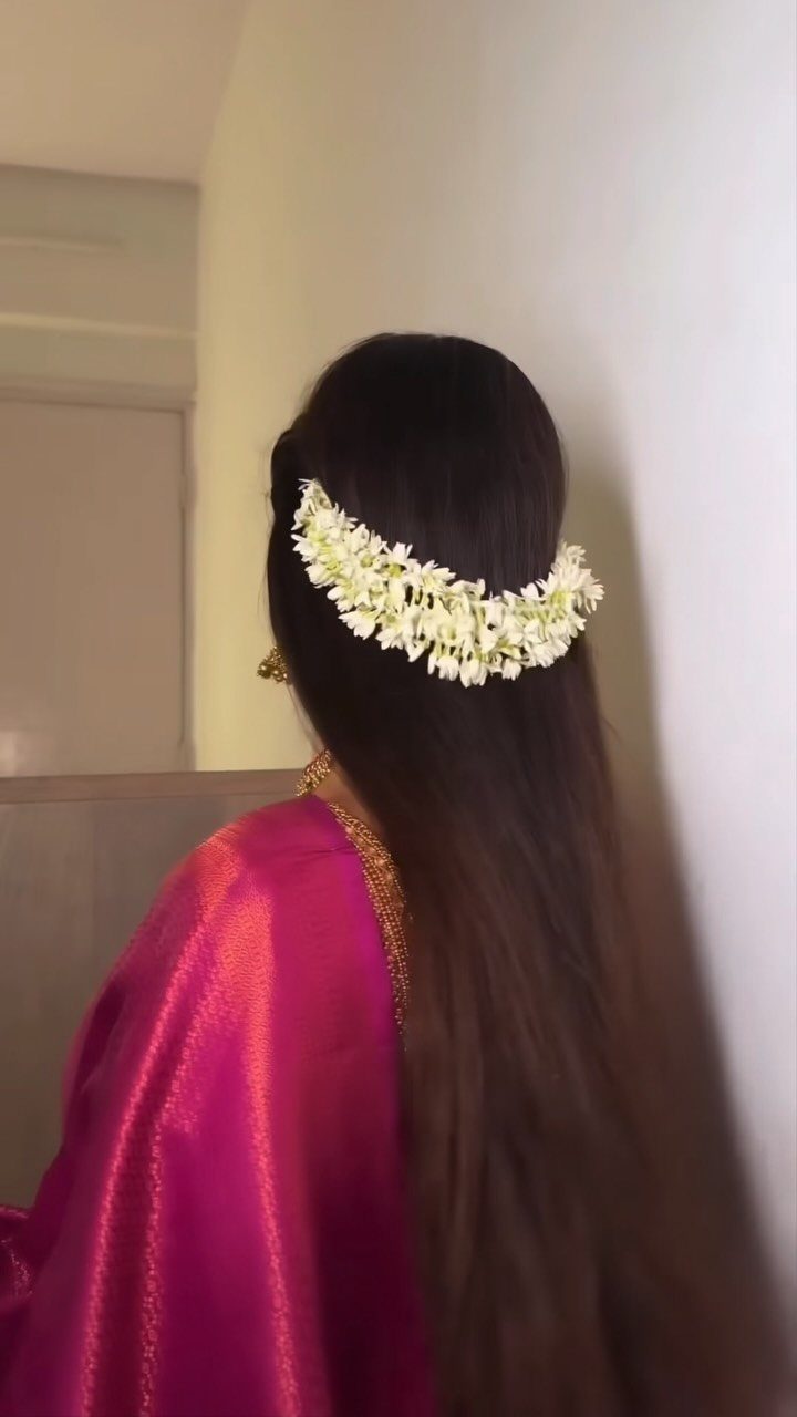 Woman with long dark hair decorated with a white jasmine flower garland and wearing pink silk.