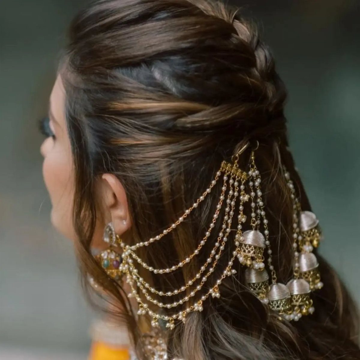 Woman with braided dark hair wearing elaborate gold pearl hair jewelry and bell ornaments.