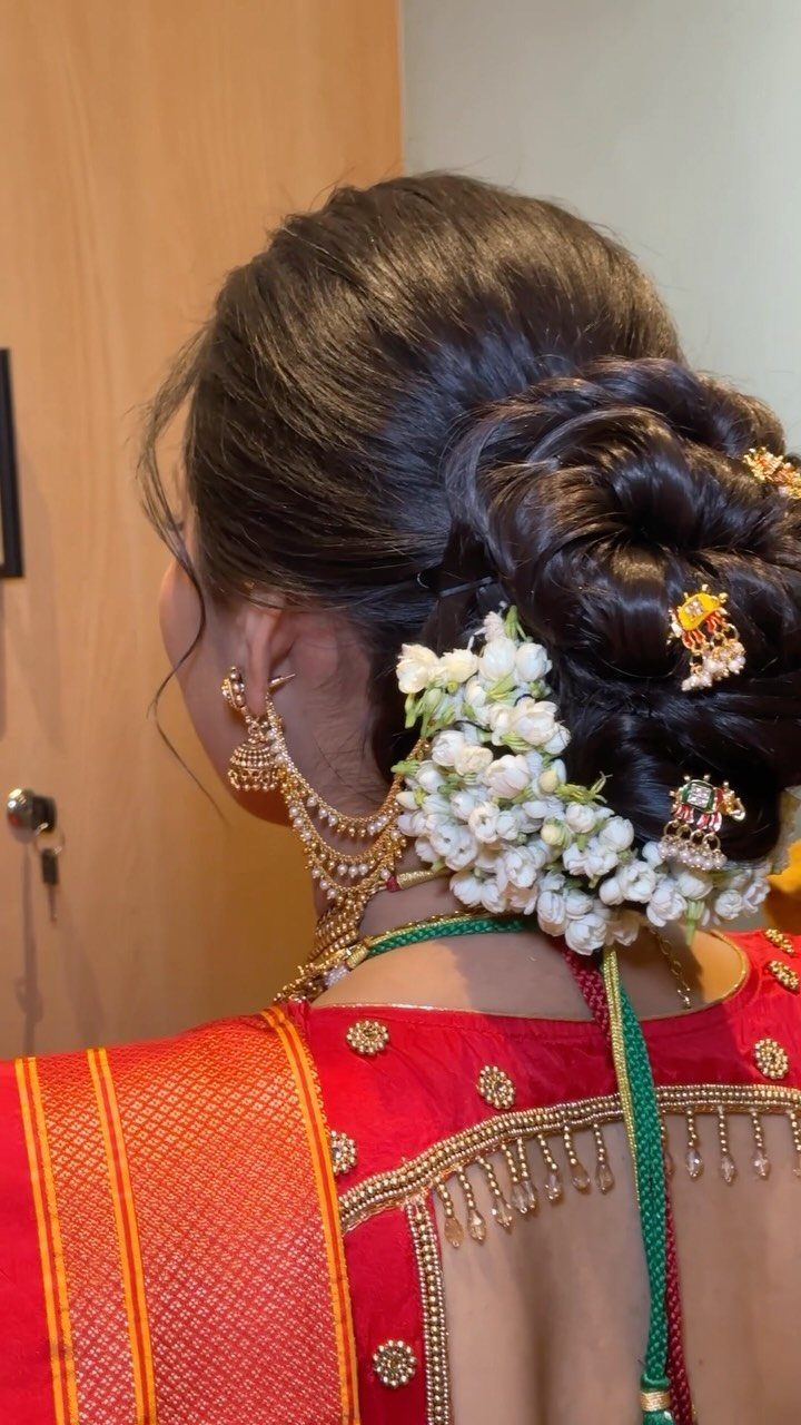A woman's dark hair styled in an intricate bun decorated with white flowers and gold ornaments.