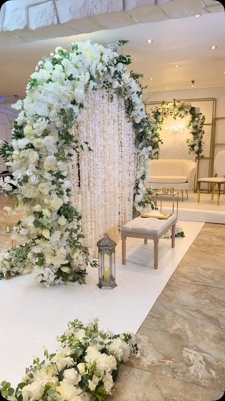 A large floral wedding archway with white flowers and greenery over a beaded backdrop.
