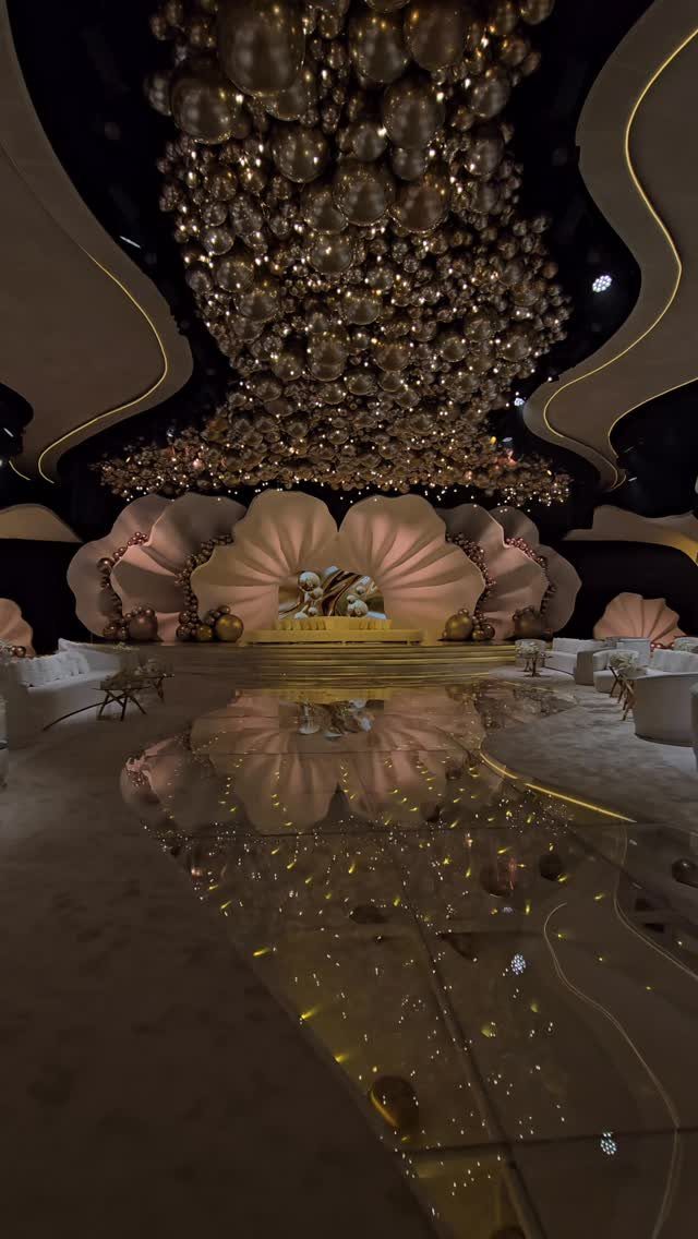 Gold and silver balloons covering a large ceiling above a reflective event hall floor.