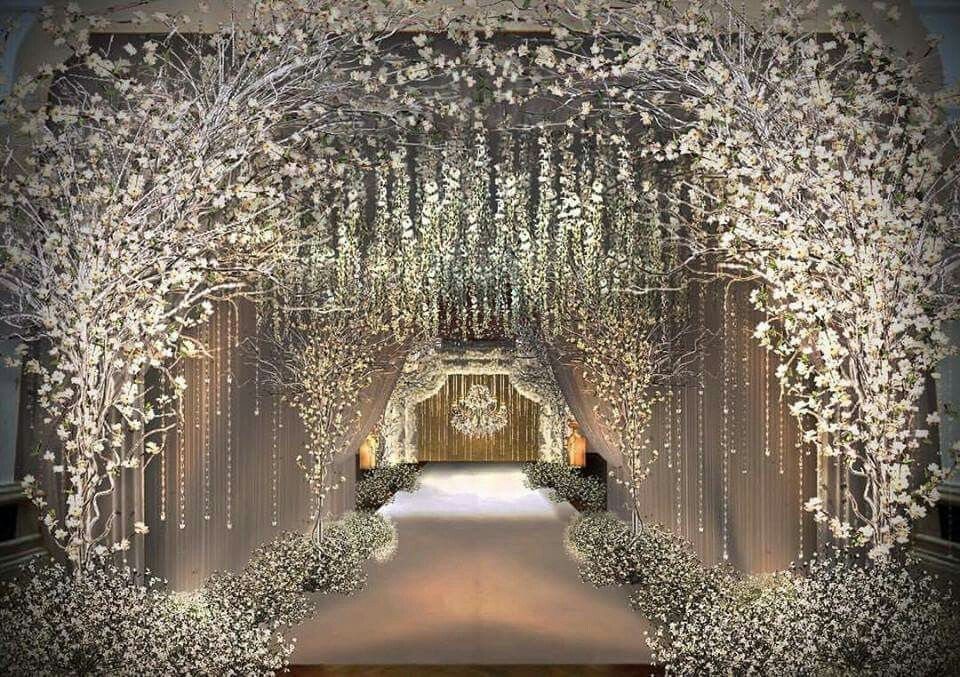 White flowering trees and hanging crystal bead strands create a decorative tunnel over a wedding aisle.