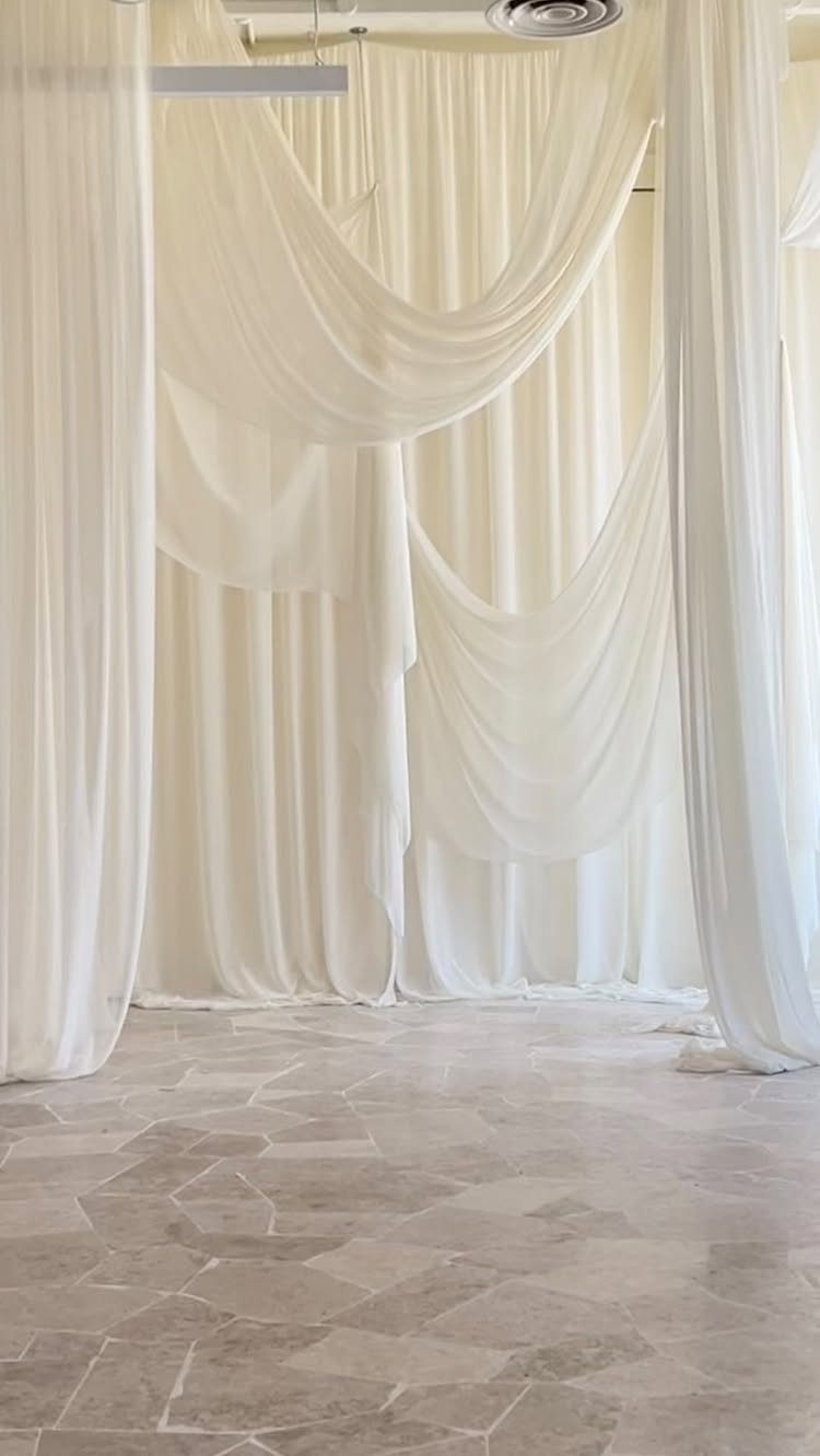 White fabric swags draped elegantly against a backdrop of flowing white curtains on a stone floor.