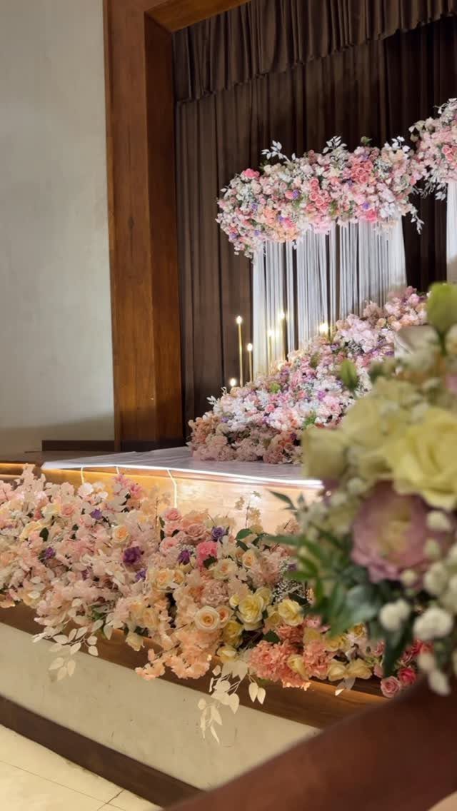 Pink and white floral arrangements decorating a wedding stage with hanging white strings and candles.
