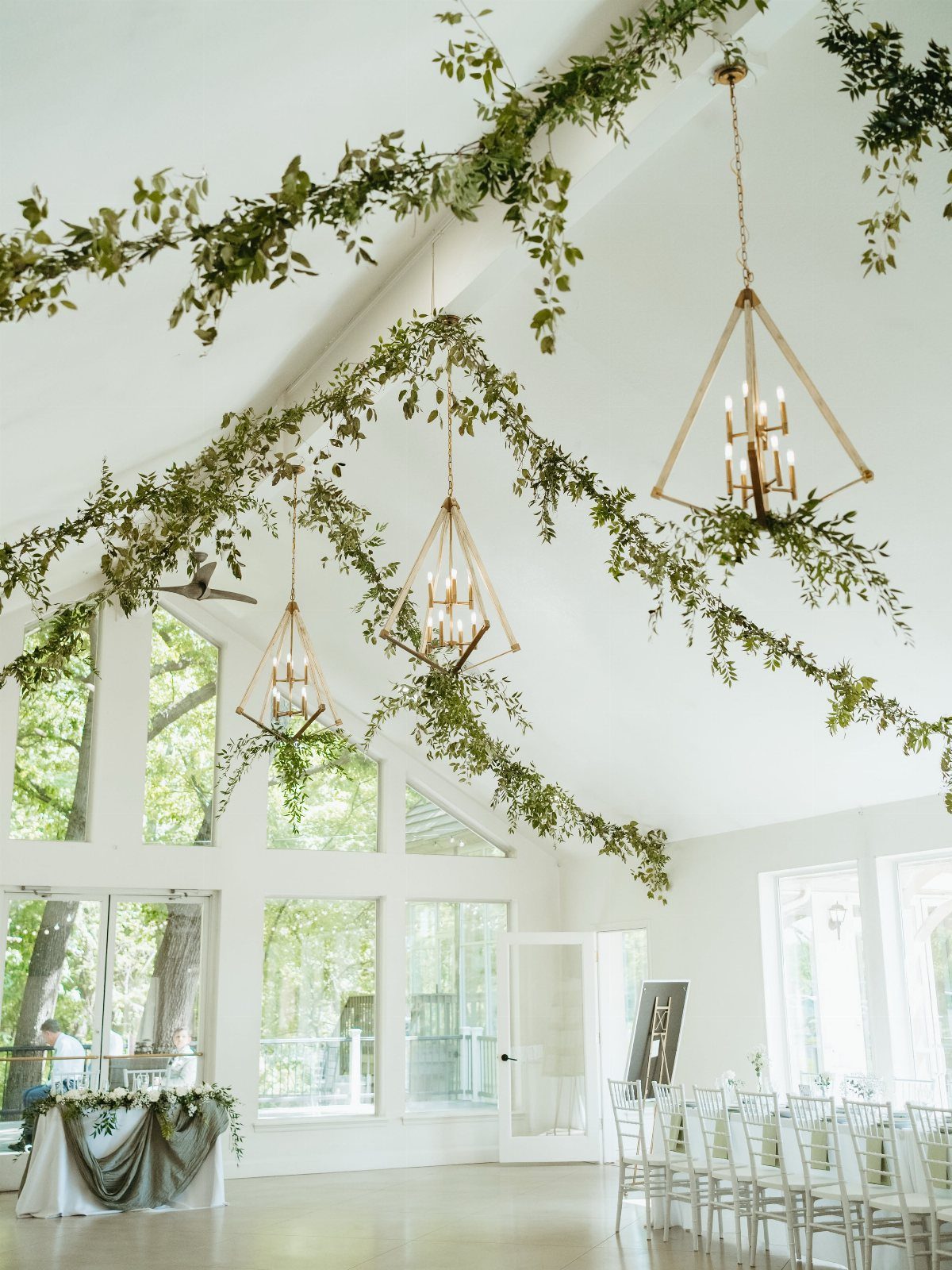 Green leafy vines draped across a white ceiling with geometric gold pendant lights hanging below.