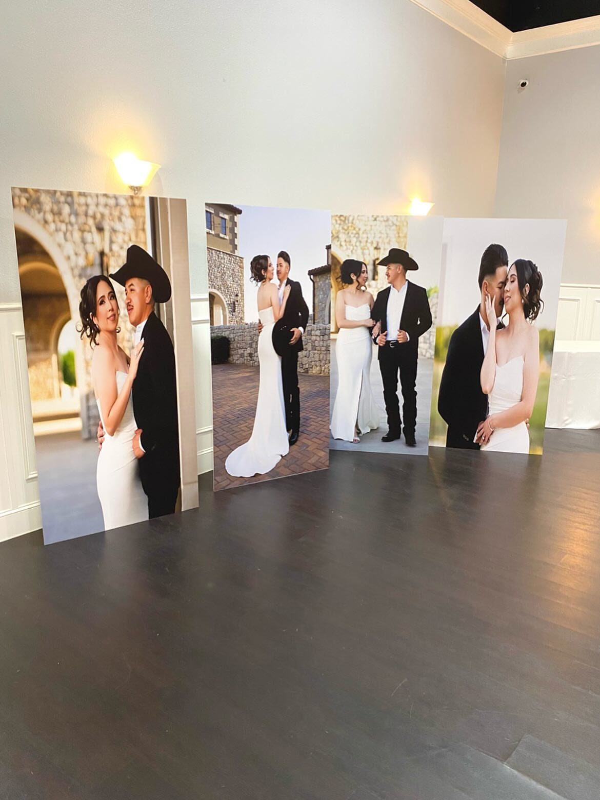 Large printed wedding portrait boards standing on a dark wooden floor indoors.