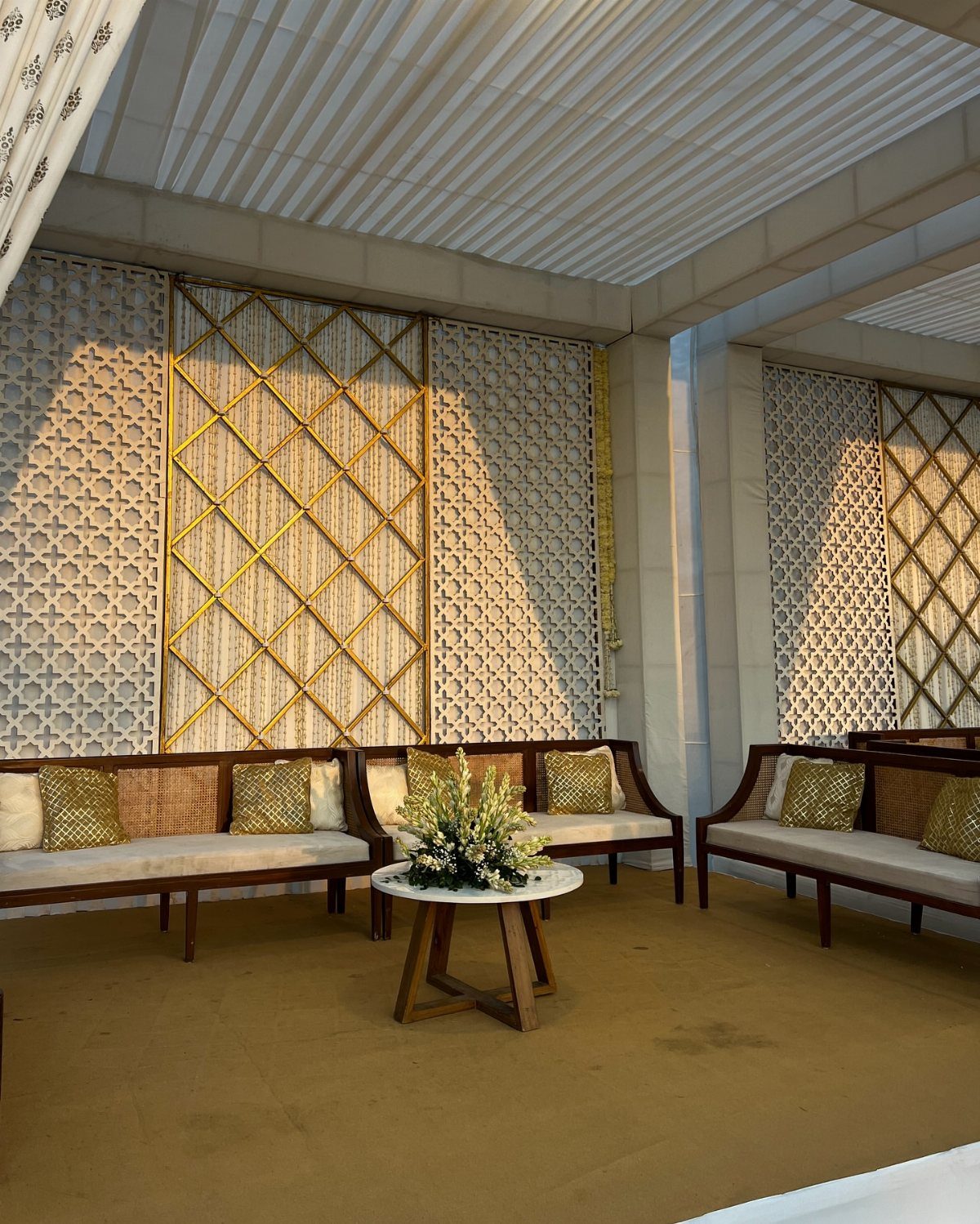 Wooden sofas with gold patterned pillows arranged around a small floral centerpiece table.