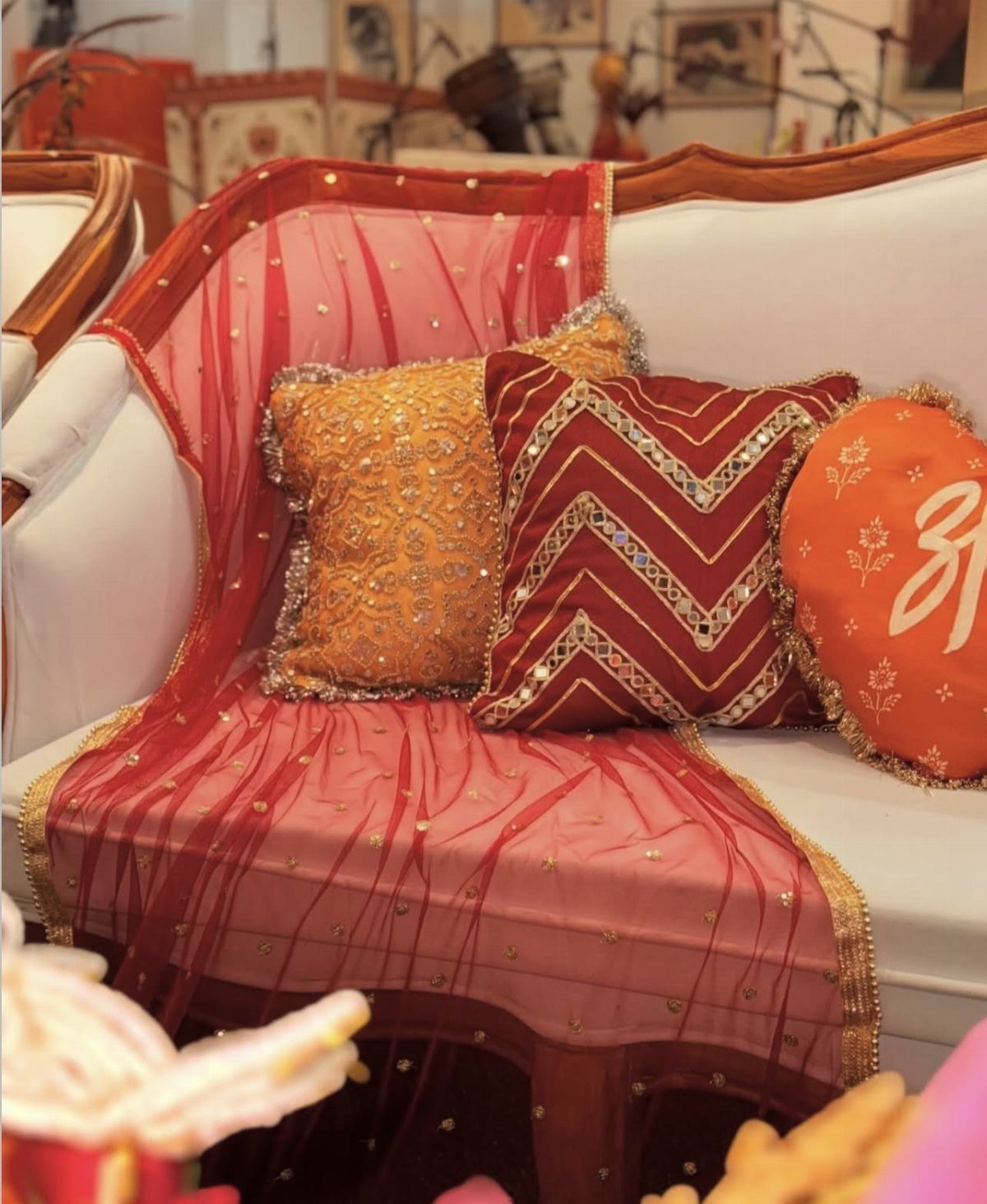 A white vintage sofa adorned with red fabric and decorative patterned pillows.