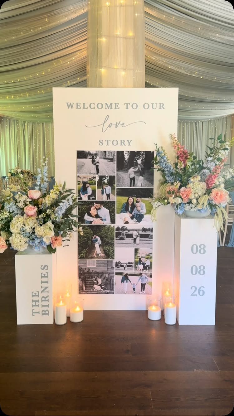 A large white wedding welcome sign featuring a photo collage and floral arrangements on pedestals.