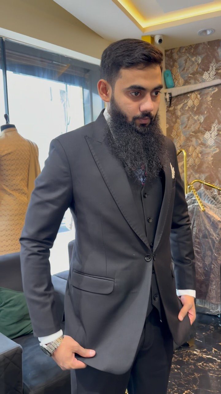 Wedding Suits for Men: 12 Groom Looks Outside Black Tie 4 A bearded man posing in a black three-piece wedding suit inside a clothing boutique.