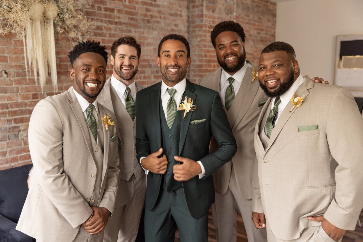 Wedding Suits for Men: 12 Groom Looks Outside Black Tie 12 Five men in coordinated beige and dark green wedding suits smiling together indoors.