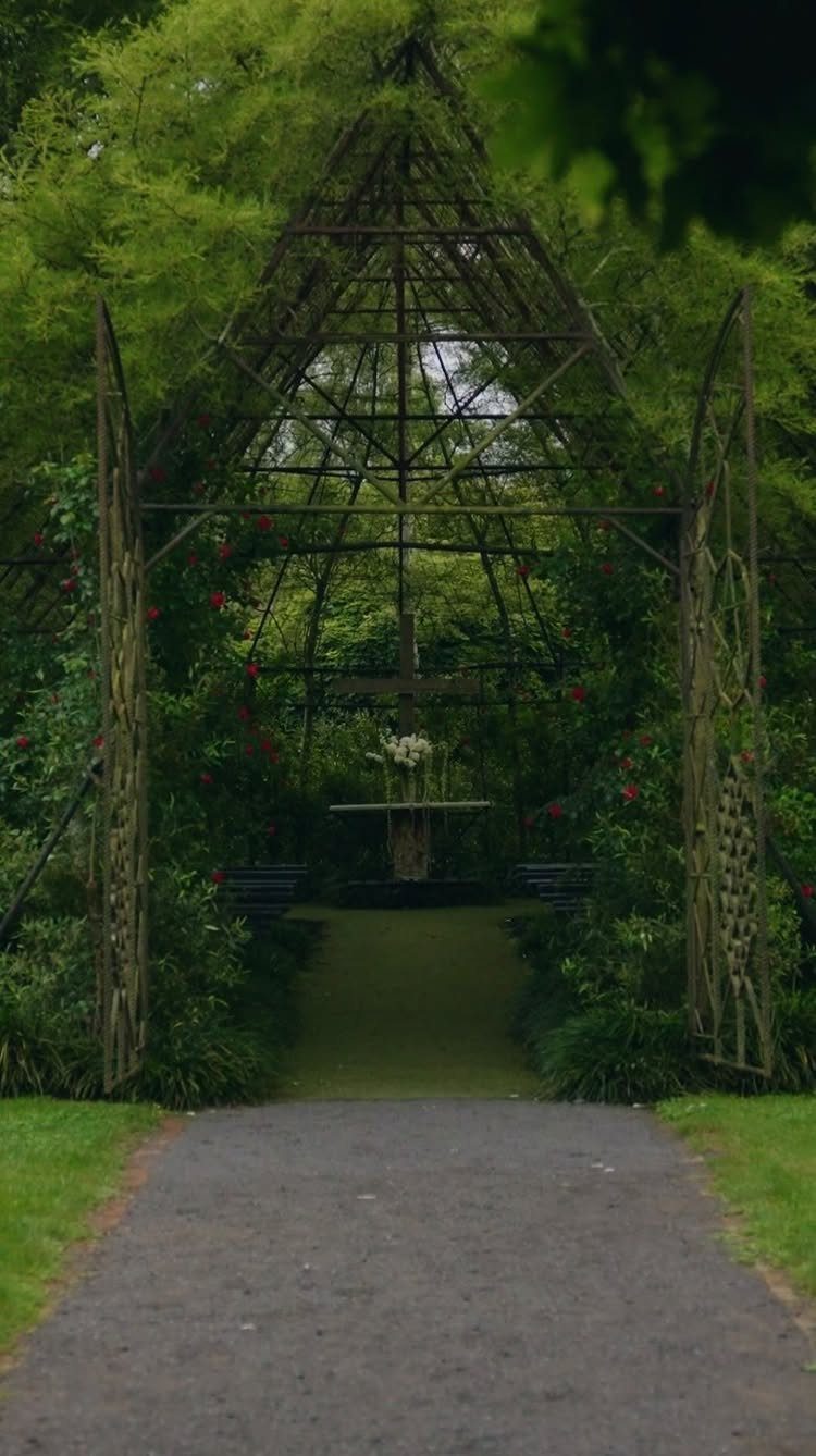 A tall metal trellis covered in green vines and red flowers in a lush forest garden.