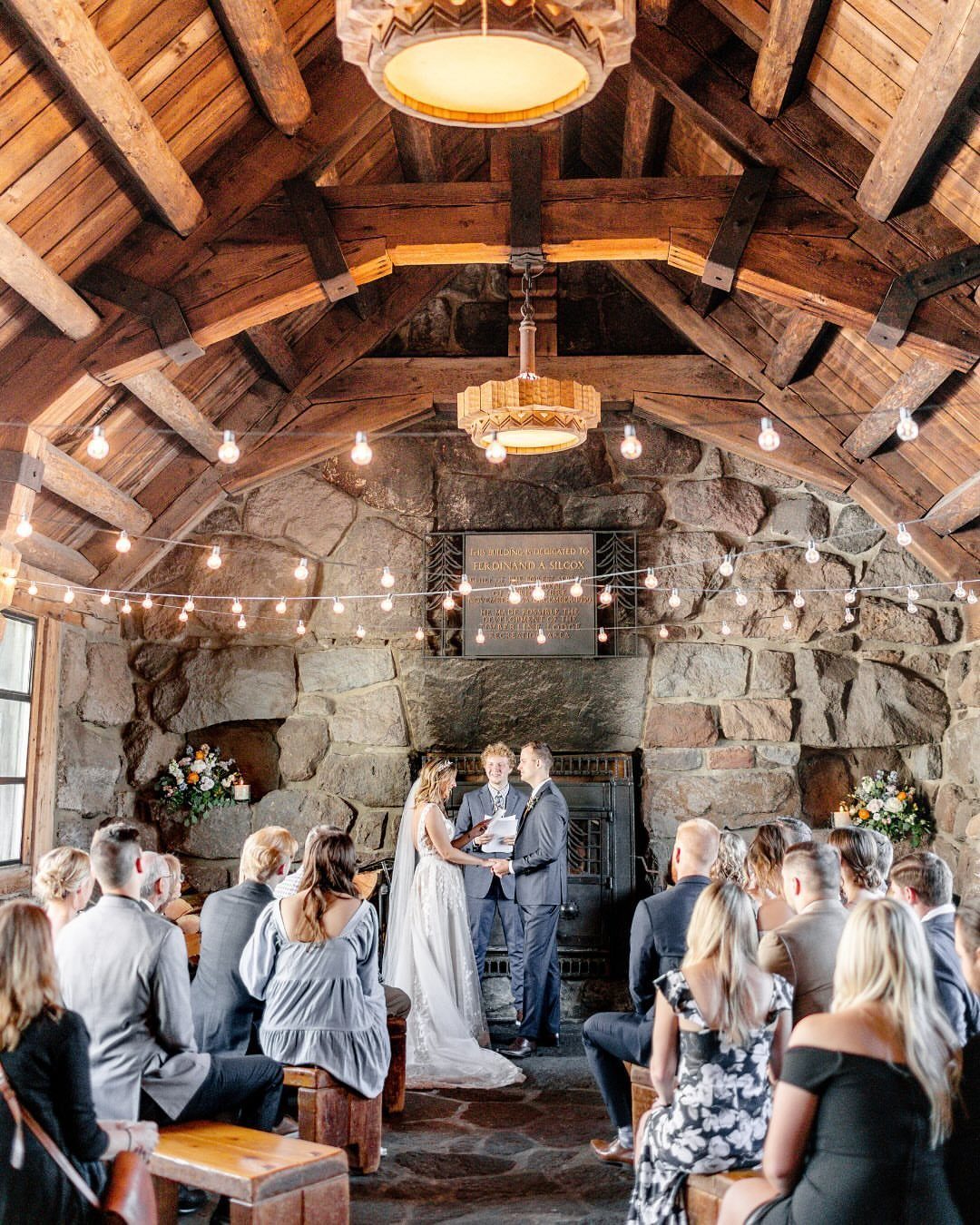 A wedding ceremony held inside a rustic lodge with stone walls and timber ceilings.