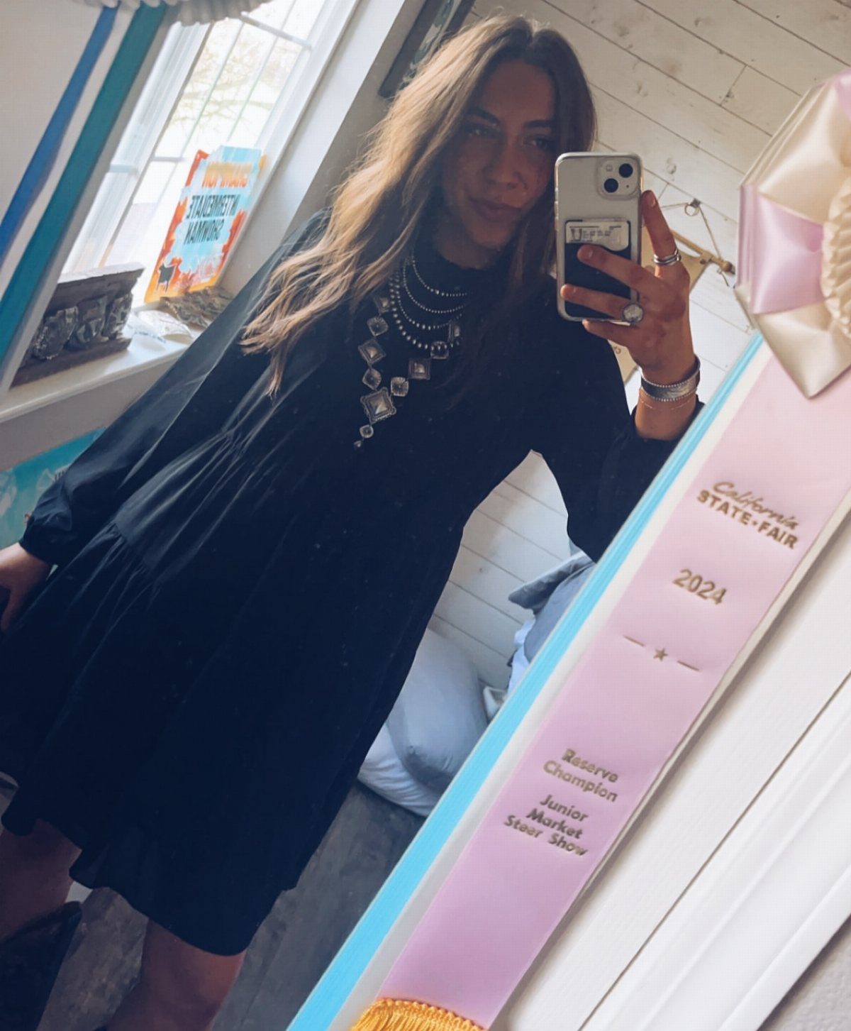 Woman in a black dress and silver statement necklace taking a mirror selfie.