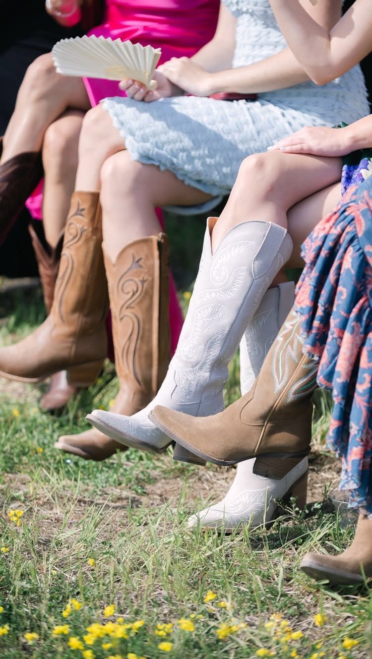 Several people sitting in a row wearing colorful dresses and various styles of western cowboy boots.