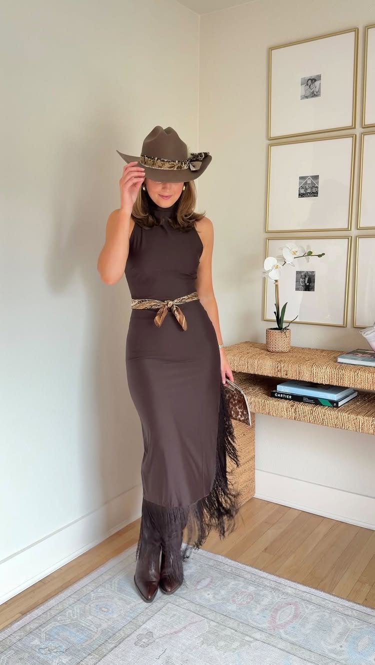 Woman posing in a brown midi dress, cowboy hat, patterned belt, and fringed cowboy boots.