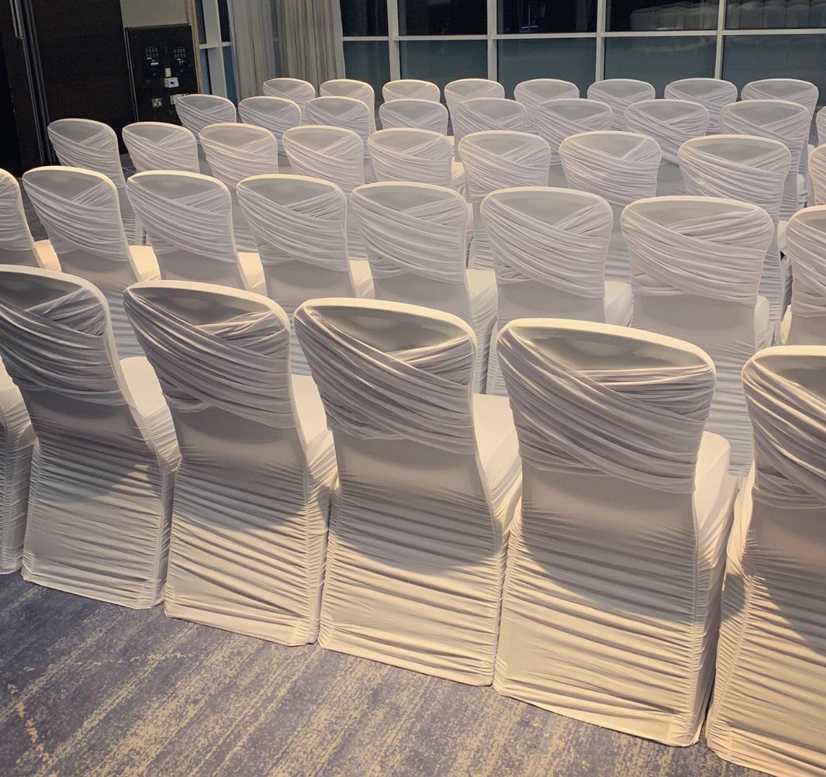 White Wedding Decorations: 10 Ideas for an Elegant Celebration 1 Rows of banquet chairs draped in elegant, pleated ivory fabric covers in an event hall.