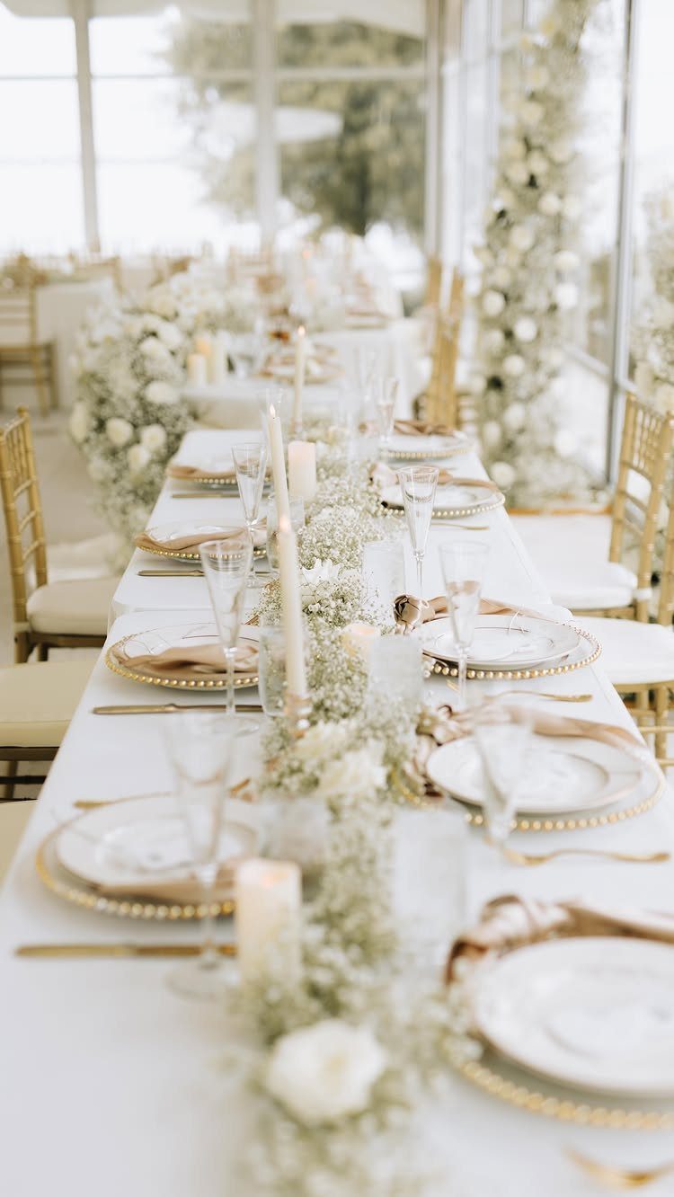 White Wedding Decorations: 10 Ideas for an Elegant Celebration 8 A long wedding reception table decorated with white floral garlands, candles, and gold-rimmed plates.
