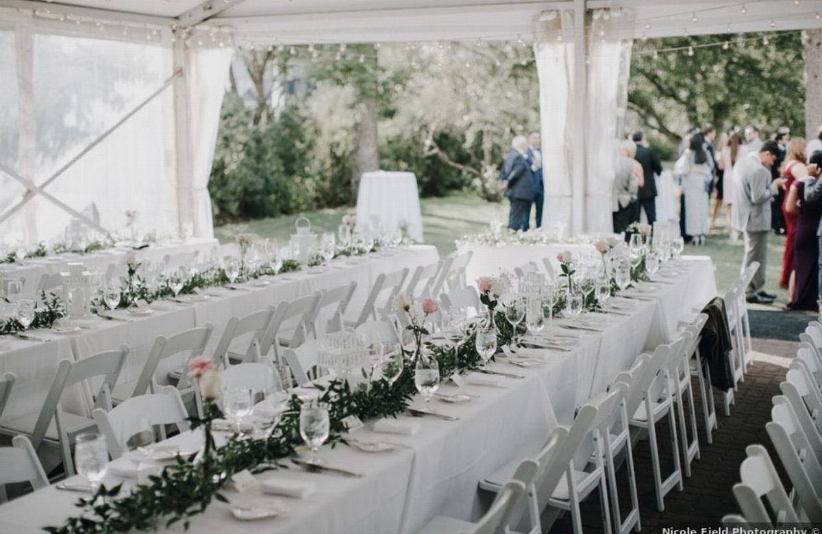White Wedding Decorations: 10 Ideas for an Elegant Celebration 5 Long banquet tables with white tablecloths and greenery garlands set under a large white wedding tent.