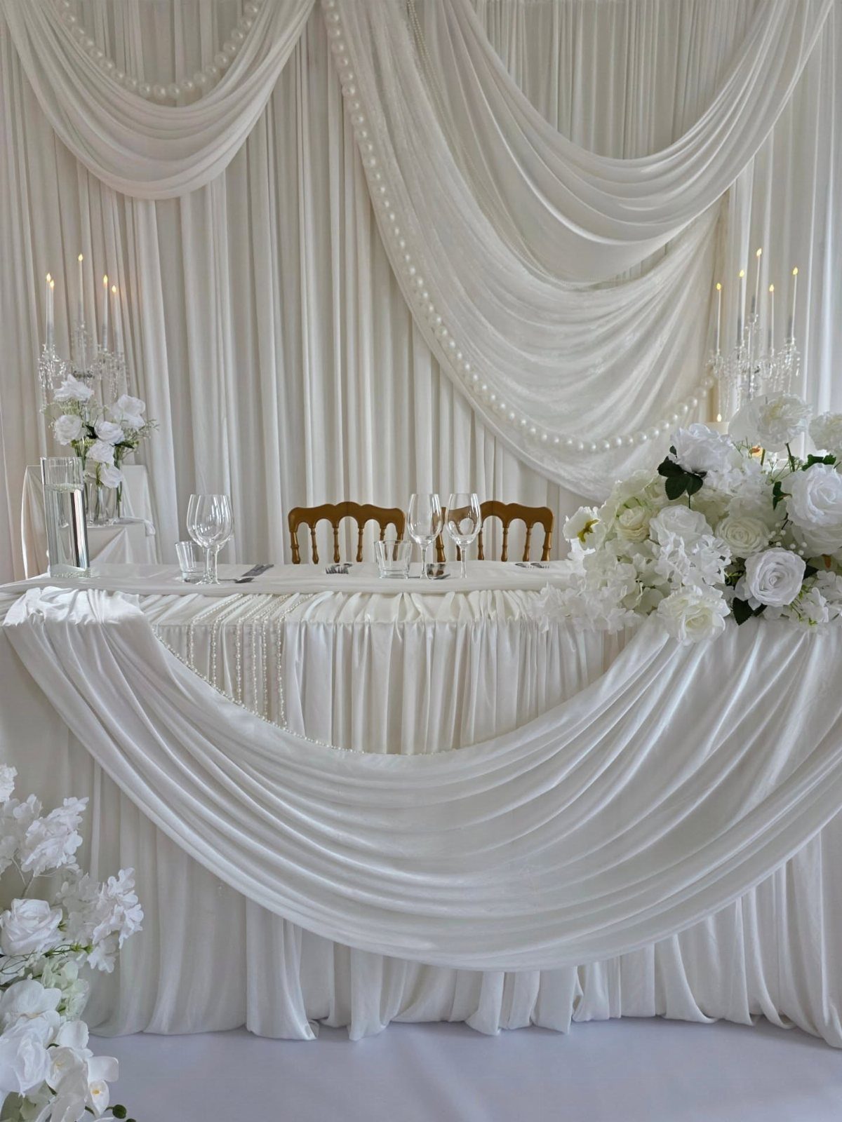 White Wedding Decorations: 10 Ideas for an Elegant Celebration 6 A wedding head table featuring white draped fabric, floral arrangements, and elegant glassware.