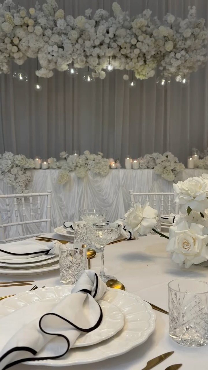 White Wedding Decorations: 10 Ideas for an Elegant Celebration 3 White wedding table setting with elegant plates, glassware, and white rose centerpieces under floral installations.