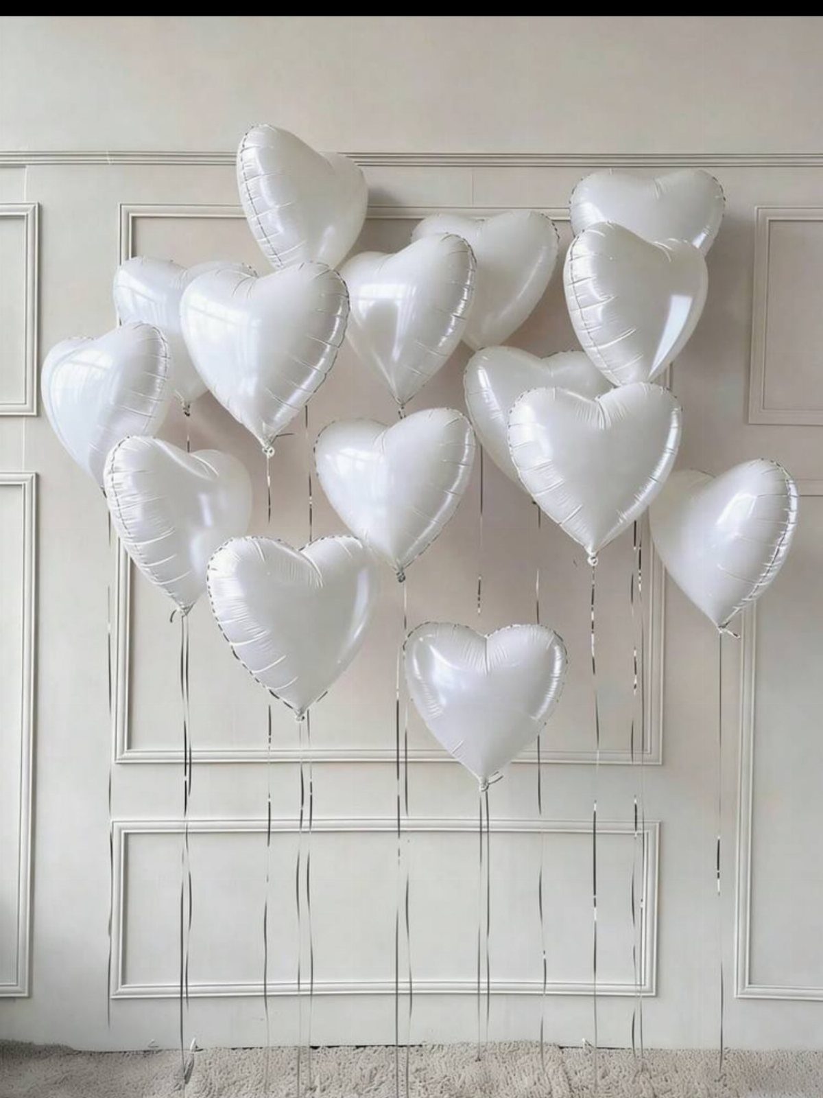 White Wedding Decorations: 10 Ideas for an Elegant Celebration 4 White heart-shaped foil balloons with silver ribbons floating against a white paneled wall.