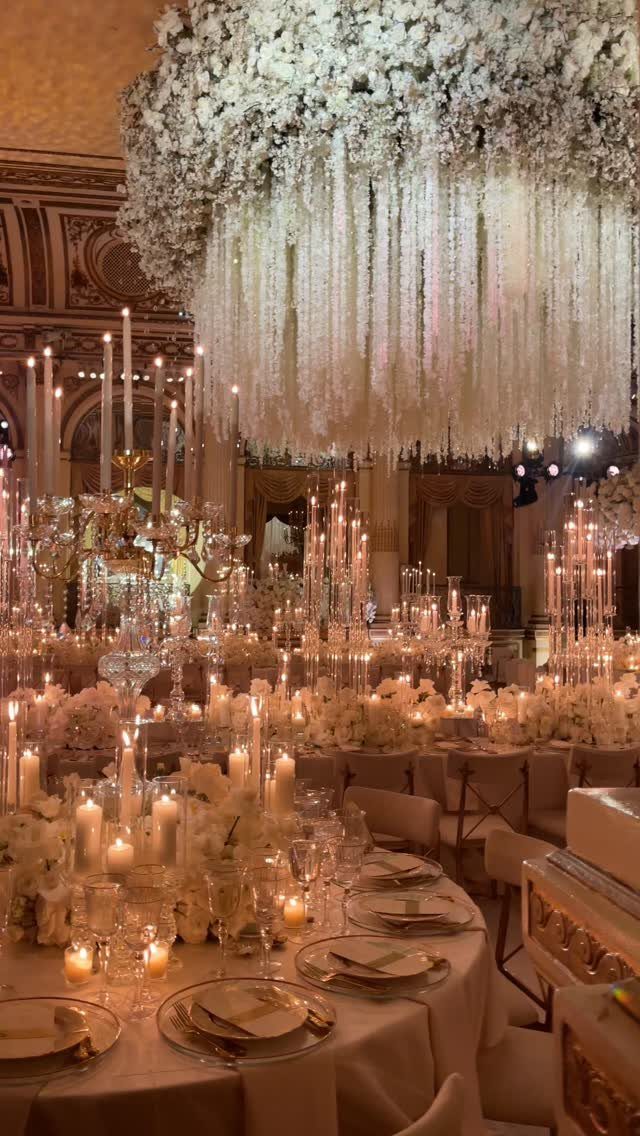 Elegant wedding reception tables with white linens, glowing candles, and a large hanging white floral installation.
