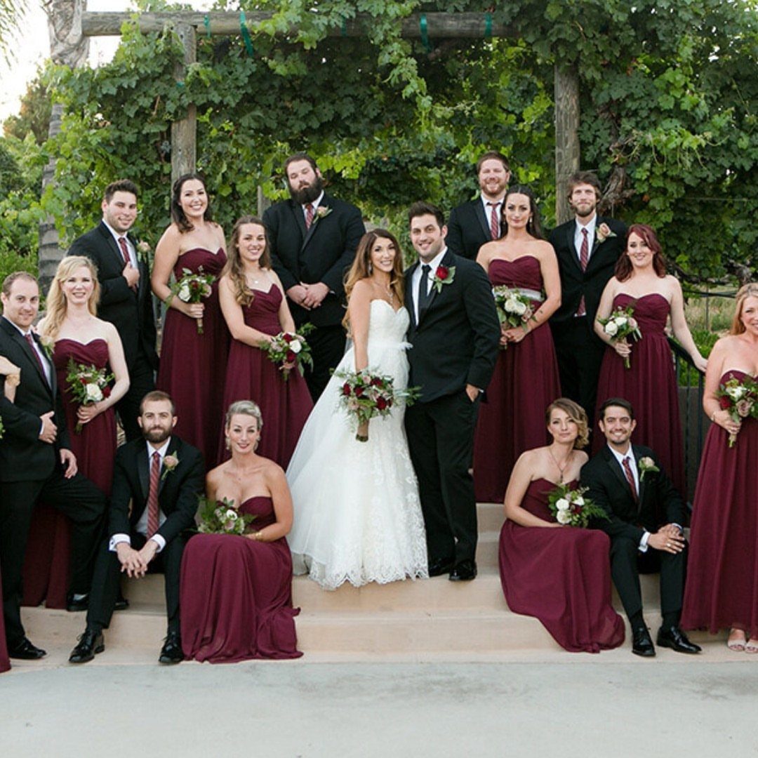 A wedding party posing with a bride in white and bridesmaids in burgundy dresses.