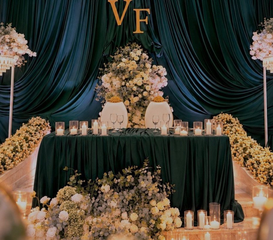 A wedding sweetheart table with a dark green tablecloth, white flowers, and glowing candles.