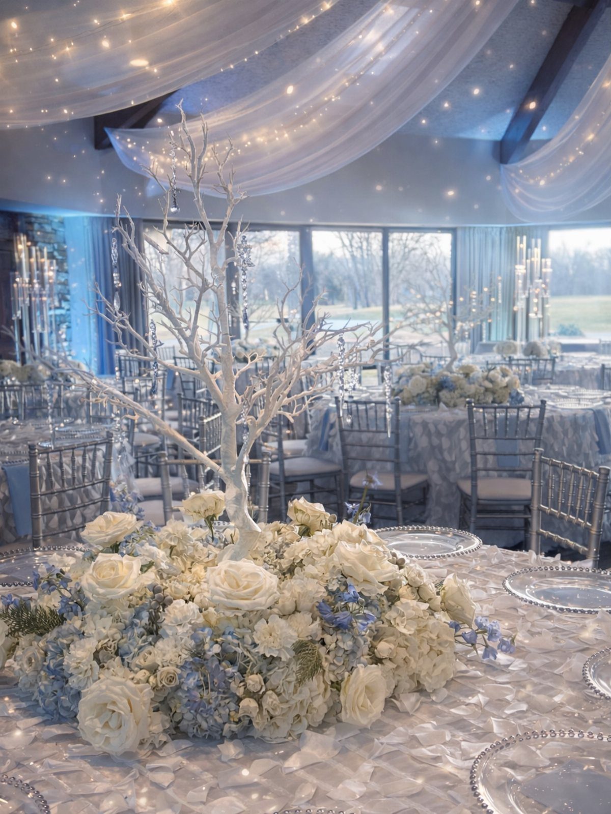 White roses and blue hydrangeas surround a white decorative branch centerpiece on a silver wedding table.