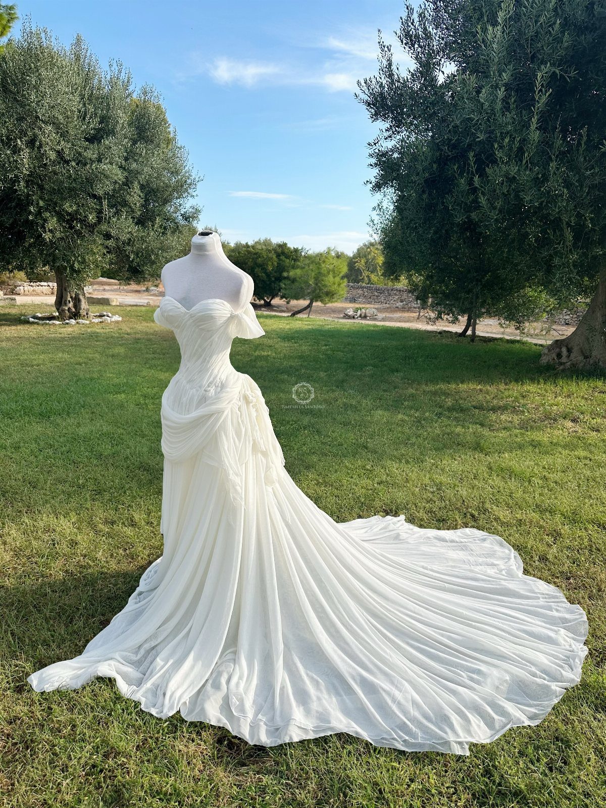 7 Enchanting Ideas for Witchy Wedding Dresses 5 A white off-the-shoulder wedding gown with a long flowing train displayed on a mannequin outdoors.