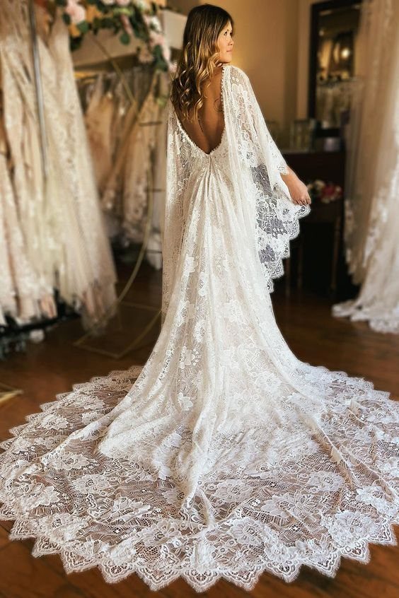 7 Enchanting Ideas for Witchy Wedding Dresses 4 A woman in a white lace wedding gown with a long, intricate train standing in a boutique.